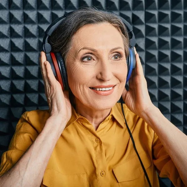Smiling older woman wearing headphones in a sound-treated booth, ready for a hearing test