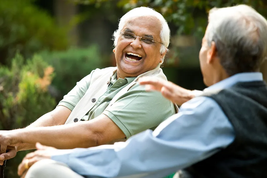 Older man laughing with a friend as they sit together outdoors