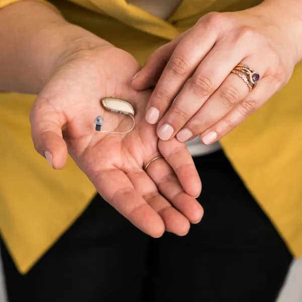 Close-up of a small receiver-in-canal (RIC) hearing aid resting in the palm of a person’s hand